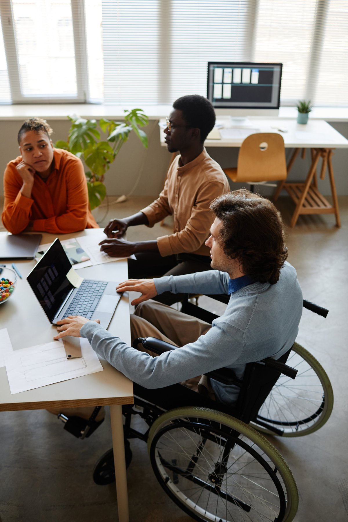 Diverse business team discussing project at meeting table with young man using wheelchair in foreground