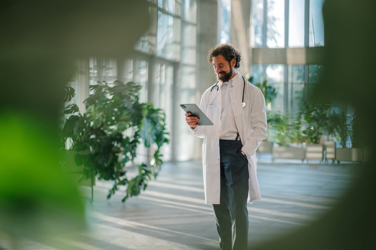 Smiling doctor walking through a modern hospital, using a digital tablet to connect and communicate in the healthcare environment - Professional disability support services in Campbelltown and Macarthur Region